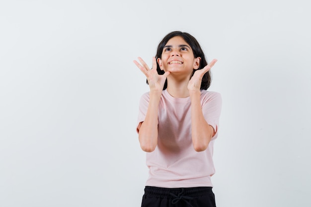 Chica joven en camiseta rosa y pantalón negro levantando las manos como tratando de sostener algo y luciendo feliz