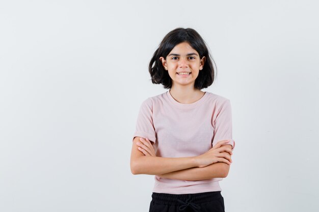 Chica joven en camiseta rosa y pantalón negro de pie con los brazos cruzados y sonriendo y mirando feliz