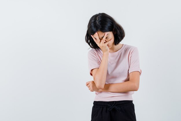 Chica joven en camiseta rosa y pantalón negro que cubre la cara con la mano y parece agotado