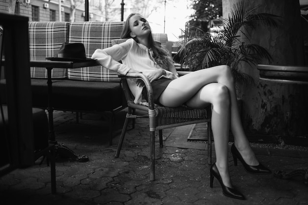Chica joven cansada sentada en el café hermosa mujer con piernas sexy descansando en el restaurante modelo sentada en un sillón en un café francés