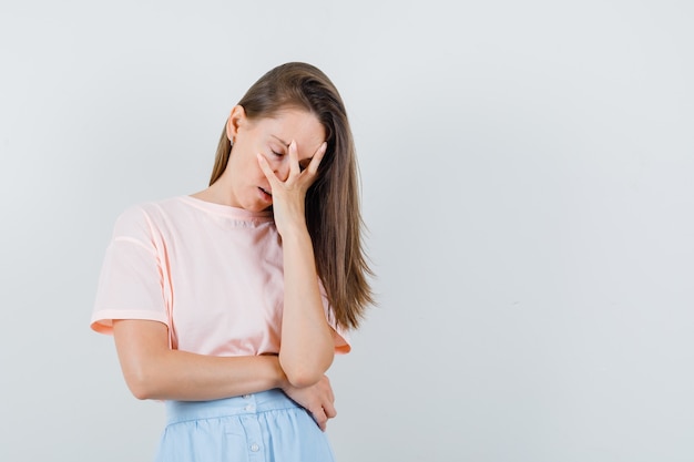 Chica joven con la cara inclinada en la mano levantada en camiseta, falda y aspecto cansado. vista frontal.