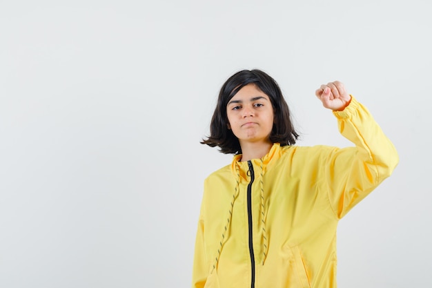 Chica joven en chaqueta de bombardero amarilla apretando el puño y mirando serio