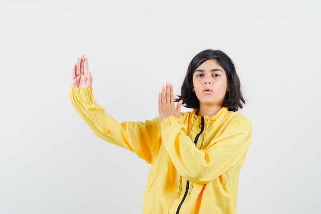 Chica joven en chaqueta de bombardero amarilla estirando las manos como mostrando escalas y mirando serio