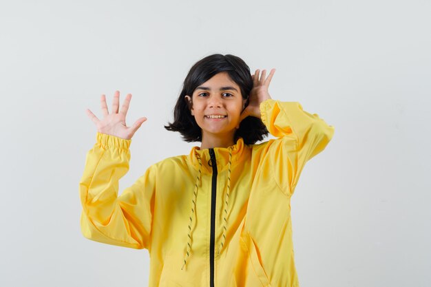 Chica joven en chaqueta de bombardero amarilla levantando las manos como saludando a alguien y mirando feliz