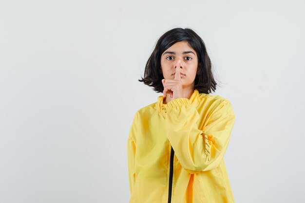 Chica joven en chaqueta de bombardero amarilla mostrando gesto de silencio y mirando serio