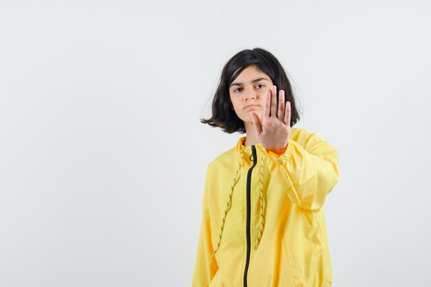 Chica joven en chaqueta de bombardero amarilla que muestra la señal de pare y parece serio