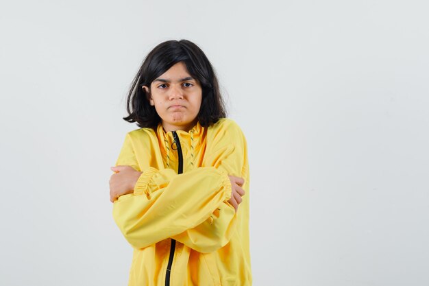 Chica joven en chaqueta de bombardero amarilla temblando de frío y mirando seria