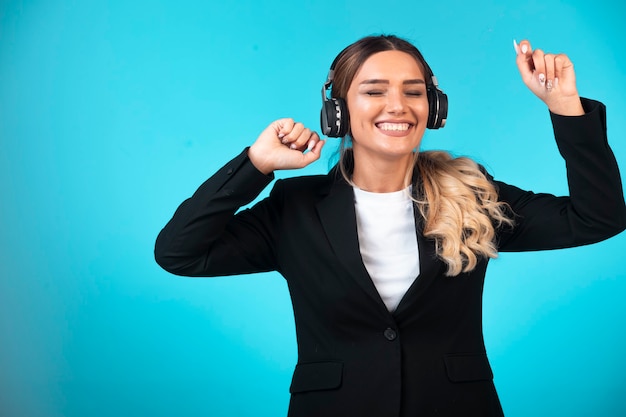 Chica joven en chaqueta negra con auriculares y bailando.