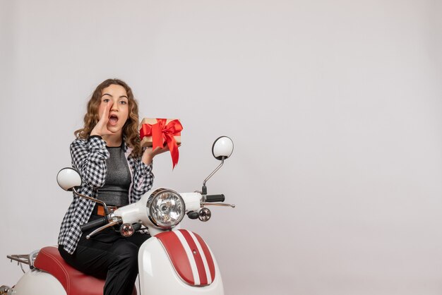 Chica joven en ciclomotor sosteniendo un regalo llamando a alguien en gris