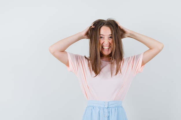 Foto gratuita chica joven cogidos de la mano en el pelo en camiseta, falda y mirando loco, vista frontal.