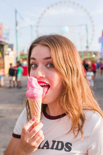 Chica joven comiendo helado en el parque de atracciones