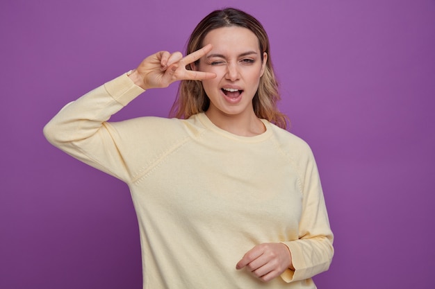 Chica joven confiada guiñando un ojo mostrando el símbolo de signo v cerca del ojo