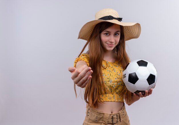 Chica joven confiada con sombrero sosteniendo un balón de fútbol estirando la mano en un espacio en blanco aislado con espacio de copia