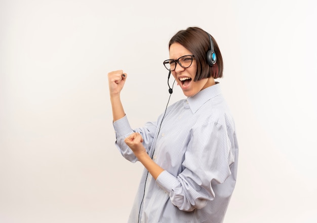 Chica joven confidente del centro de llamadas con gafas y auriculares de pie en la vista de perfil gesticulando fuerte aislado en blanco con espacio de copia