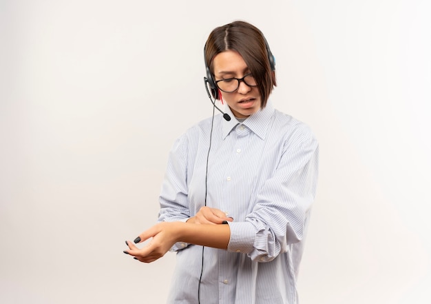 Chica joven confidente del centro de llamadas con gafas y auriculares retocando y mirando su manga aislada en blanco con espacio de copia