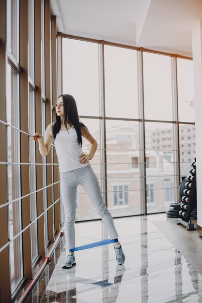 chica joven y delgada con una camisa blanca y polainas grises dedicadas a los deportes en el gimnasio