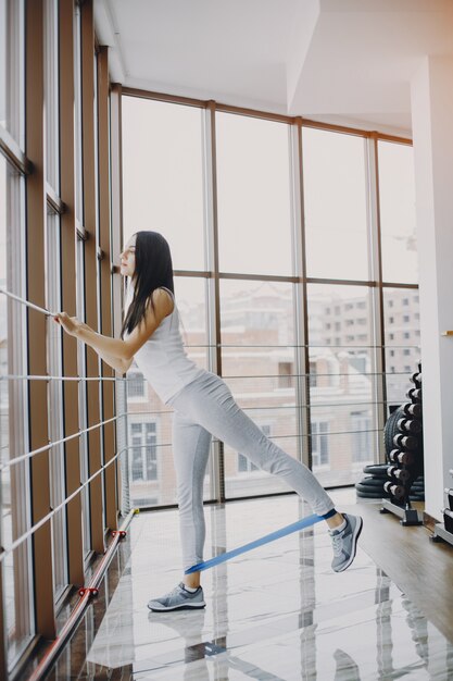 chica joven y delgada con una camisa blanca y polainas grises dedicadas a los deportes en el gimnasio