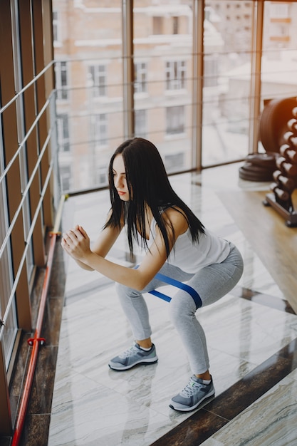 chica joven y delgada con una camisa blanca y polainas grises dedicadas a los deportes en el gimnasio