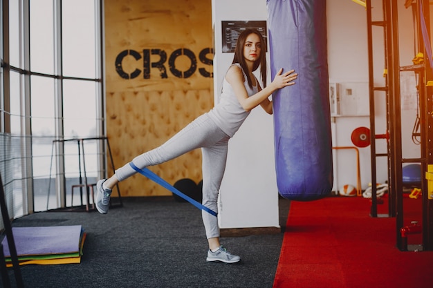 chica joven y delgada con una camisa blanca y polainas grises dedicadas a los deportes en el gimnasio