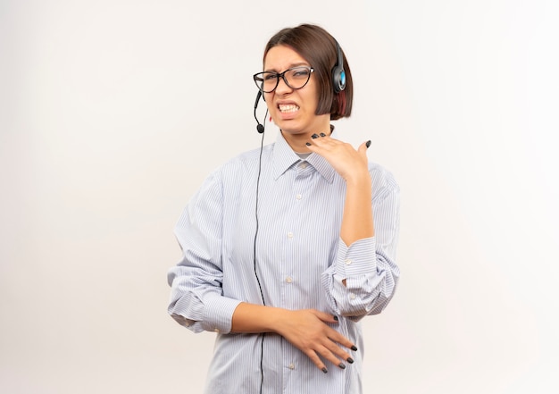 Chica joven descontenta del centro de llamadas con gafas y auriculares manteniendo la mano en el aire aislado sobre fondo blanco con espacio de copia