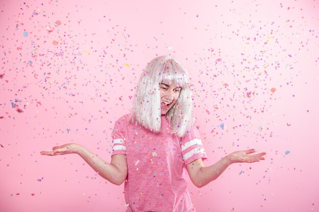 Chica joven divertida con cabello plateado da una sonrisa y emoción sobre fondo rosa con confeti.