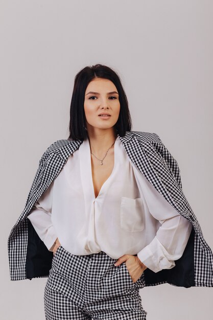 Chica joven elegante atractiva en ropa de negocios posando sobre fondo claro en estudio. Concepto de ropa elegante y sofisticación.