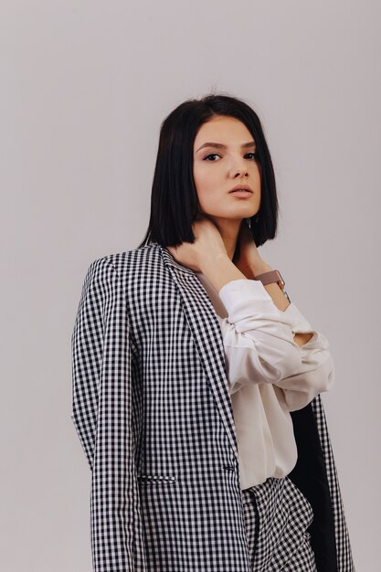 Chica joven elegante atractiva en ropa de negocios posando sobre fondo claro en estudio. Concepto de ropa elegante y sofisticación.