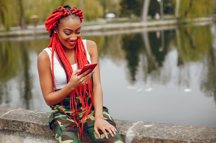 Foto gratuito una chica joven y elegante de piel oscura con rastas rojas caminando en el parque de verano cerca del río