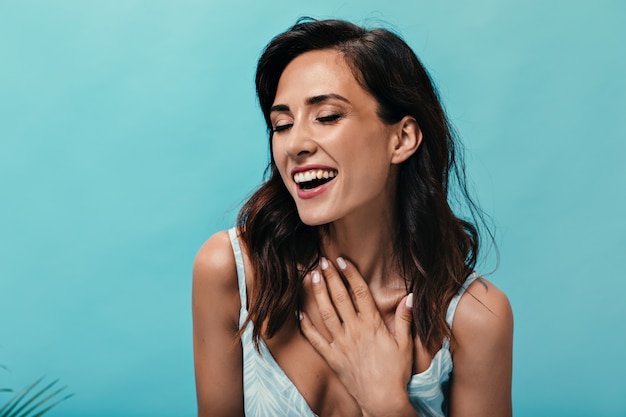 Chica joven y elegante se ríe sobre fondo azul aislado. Mujer sonriente con pelo corto ondulado oscuro en una camiseta amarilla posando.