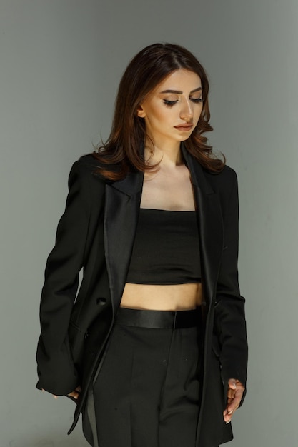 Chica joven con elegante traje negro y soporte de fondo gris Foto de alta calidad