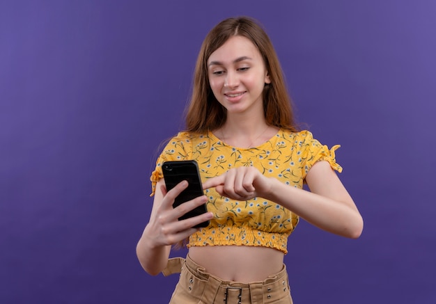 Foto gratuita chica joven emocionada sosteniendo el teléfono móvil y poniendo el dedo sobre él en el espacio púrpura aislado con espacio de copia