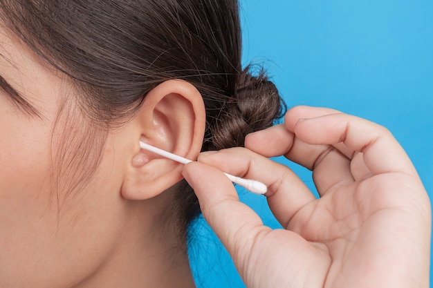 La chica joven es la oreja que escoge con la esponja de algodón en la pared azul, estudio.