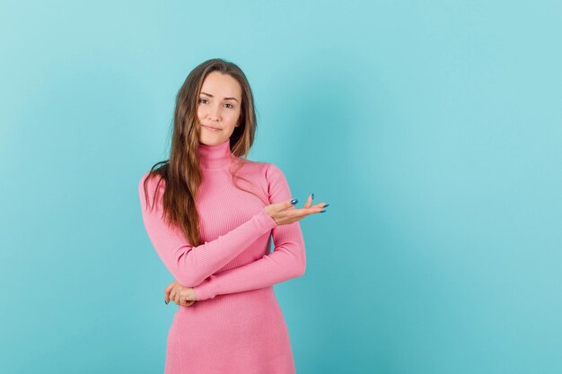 La chica joven está apuntando a la derecha con la mano sobre fondo azul.