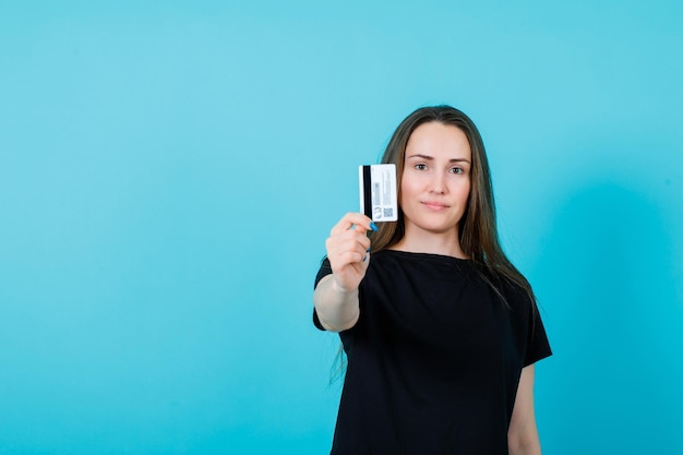 Chica joven está mostrando la tarjeta de crédito a la cámara sobre fondo azul.