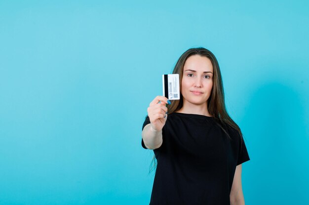Chica joven está mostrando la tarjeta de crédito a la cámara sobre fondo azul.