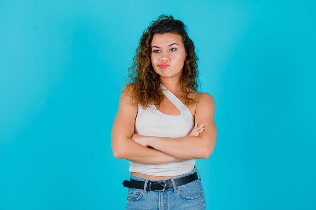 La chica joven está pensando cruzando los brazos sobre fondo azul.