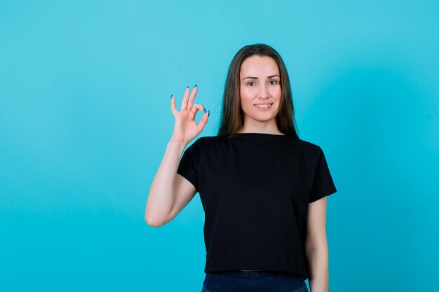 La chica joven está sonriendo mostrando un gesto correcto en el fondo azul