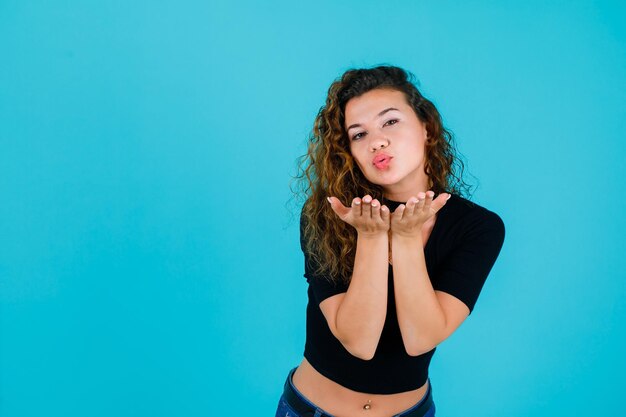 Chica joven está soplando un beso a la cámara sobre fondo azul.