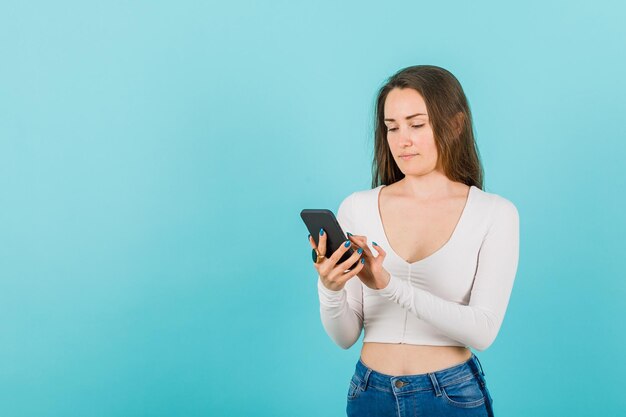 La chica joven está trabajando en un teléfono inteligente con fondo azul