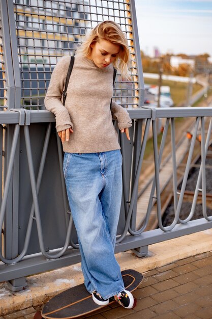 Chica joven con estilo urbano caminando con monopatín. Retrato al aire libre de modelo de mujer deportiva activa. Estilo de vida saludable. Deportes extremos. Look de moda, retrato hipster al aire libre. Close Up retrato de un prett