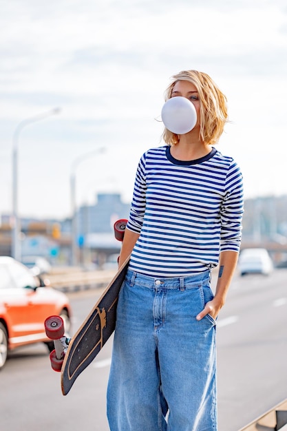 Chica joven con estilo urbano caminando con monopatín. Retrato al aire libre de modelo de mujer deportiva activa. Estilo de vida saludable. Deportes extremos. Look de moda, retrato hipster al aire libre. Close Up retrato de un prett