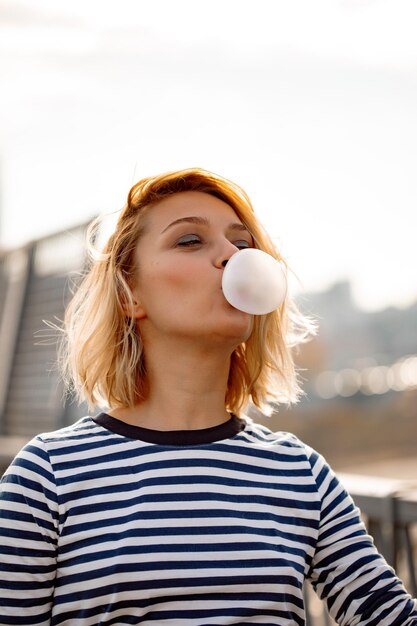 Chica joven con estilo urbano. Retrato emocional al aire libre de modelo de mujer activa. Estilo de vida saludable. Look de moda, retrato hipster al aire libre. Primer plano retrato de una chica joven y bonita masticando chicle.