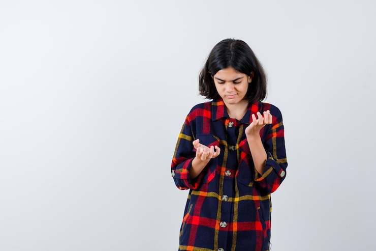 Foto gratuito chica joven estirando la mano como sosteniendo algo y mirándolo con camisa a cuadros y mirando enfocado. vista frontal.