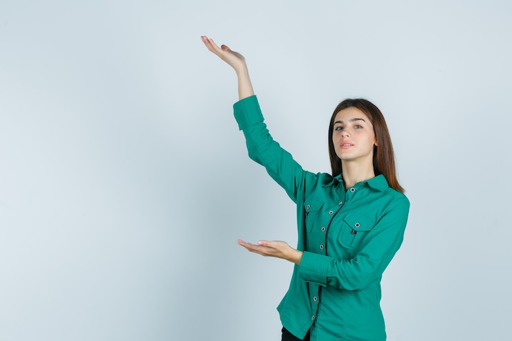 Foto gratuito chica joven estirando las manos como sosteniendo algo en blusa verde, pantalón negro y mirando serio, vista frontal.