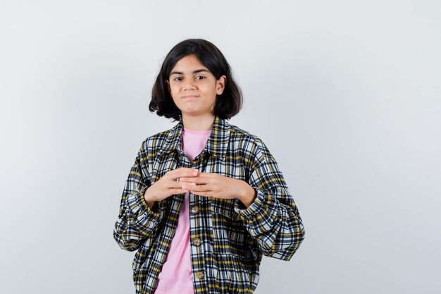 Chica joven estrechando las manos en camisa a cuadros y camiseta rosa y luciendo lindo. vista frontal.