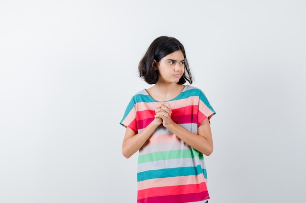 Chica joven estrechando las manos, mirando a otro lado en camiseta a rayas de colores y luciendo bonita. vista frontal.