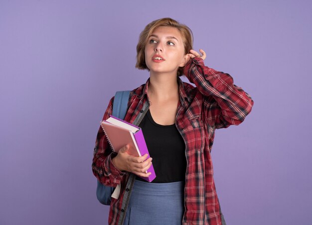 Chica joven estudiante eslava confiada con mochila sostiene el libro y el cuaderno mira al lado