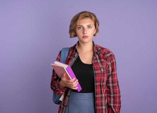 Chica joven estudiante eslava confiada con mochila sostiene libro y cuaderno