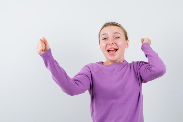 Chica joven feliz levantando sus puños sobre fondo blanco.