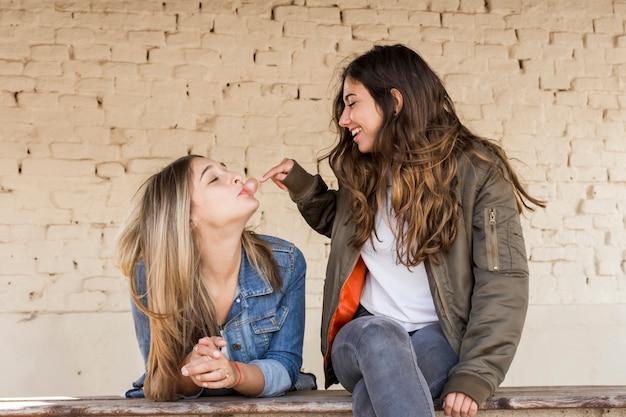 Chica joven feliz que toca una burbuja soplada por su amigo con el chicle